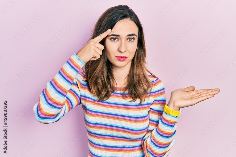 Young hispanic girl wearing casual clothes confused and annoyed with open palm showing copy space and pointing finger to forehead. think about it. Young hispanic girl wearing casual clothes confused and annoyed with open palm showing copy space and pointing finger to forehead. think about it.