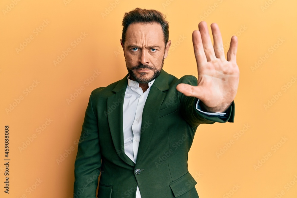 Middle age man wearing business suit doing stop sing with palm of the hand. warning expression with negative and serious gesture on the face. Middle age man wearing business suit doing stop sing with palm of the hand. warning expression with negative and serious gesture on the face.