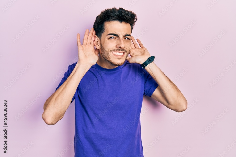 Young hispanic man wearing casual t shirt trying to hear both hands on ear gesture, curious for gossip. hearing problem, deaf