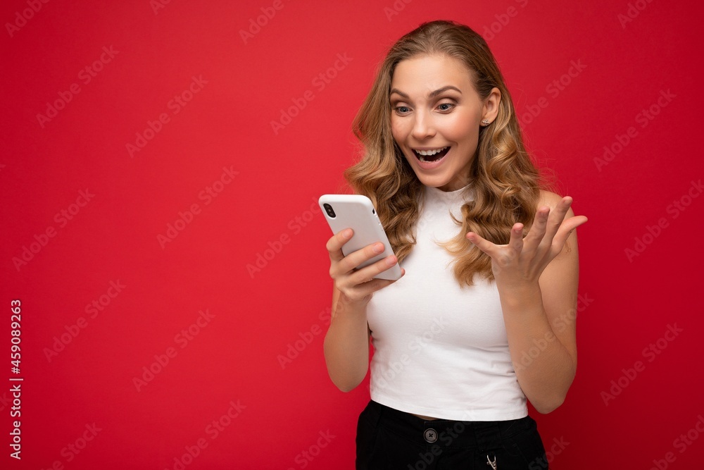 Photo of attractive crazy amazed surprised young woman wearing casual stylish clothes standing isolated over background with copy space holding and using mobile phone looking at device display Photo of attractive crazy amazed surprised young woman wearing casual stylish clothes standing isolated over background with copy space holding and using mobile phone looking at device display