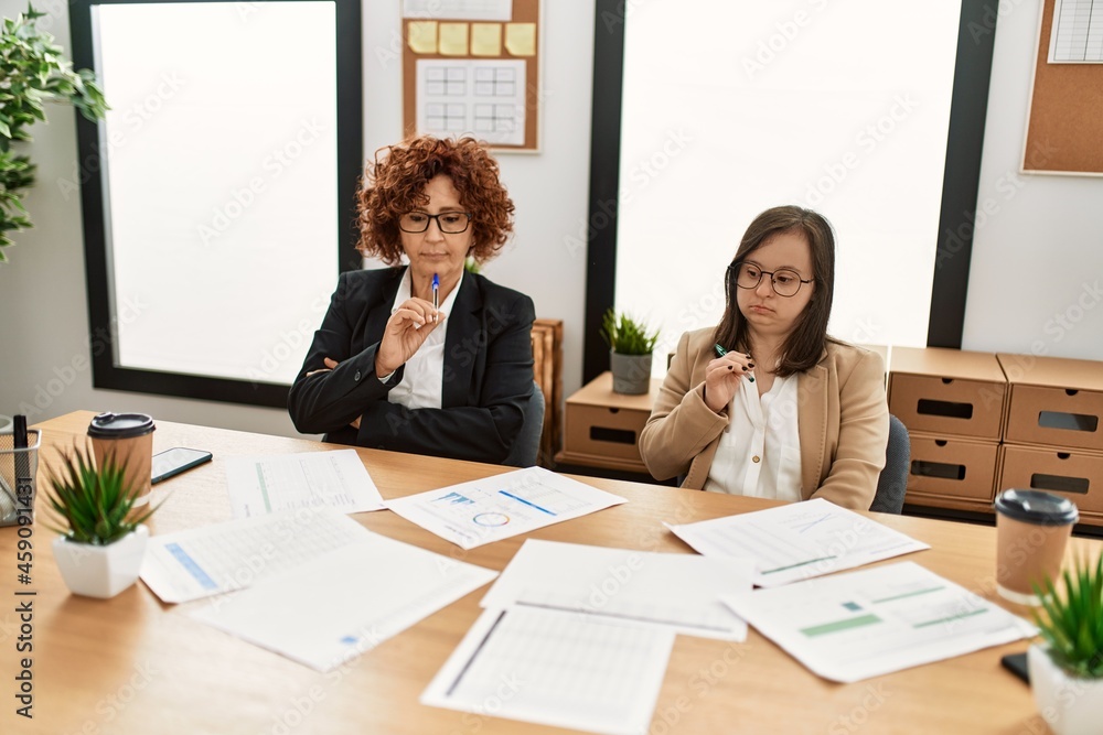 Group of two women working at the office. Mature woman and down syndrome girl working at inclusive teamwork. Group of two women working at the office. Mature woman and down syndrome girl working at inclusive teamwork.