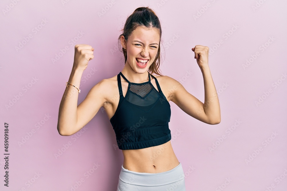 Young brunette woman wearing sportswear screaming proud, celebrating victory and success very excited with raised arms