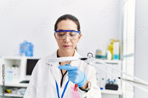 Young hispanic woman wearing scientist uniform working at laboratory