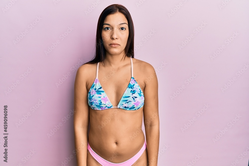 Naklejka premium Young latin woman wearing bikini with serious expression on face. simple and natural looking at the camera.