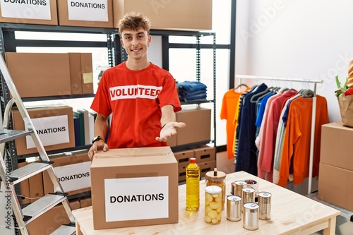 Young caucasian man volunteer holding donations box smiling cheerful offering palm hand giving assistance and acceptance.