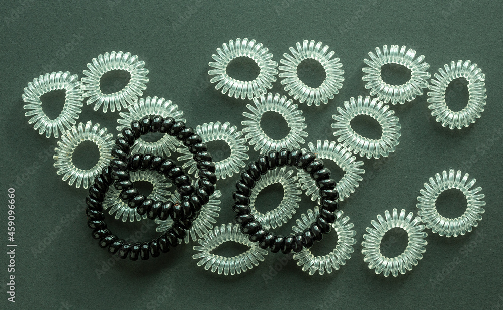 Hair ties, modern invisible hair tie. Set of black and transparent plastic telephone cord scrunchies. Green, white and grey background.