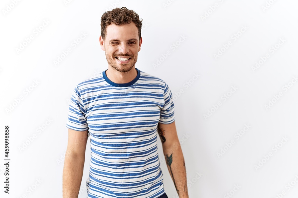 Obraz premium Handsome young man standing over isolated background winking looking at the camera with sexy expression, cheerful and happy face.