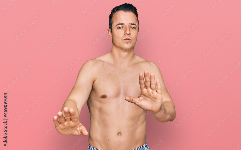 Handsome young man wearing swimwear shirtless moving away hands palms showing refusal and denial with afraid and disgusting expression. stop and forbidden.