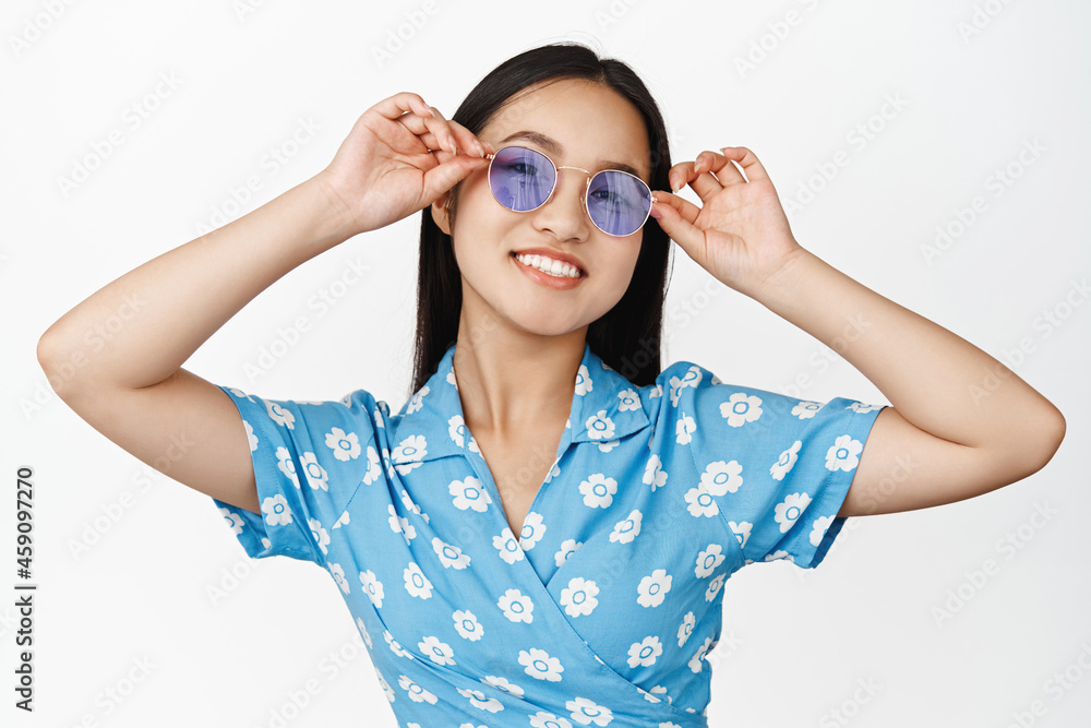 Portrait of stylish asian woman in sunglasses, smiling and looking happy, standing in dress over white background Portrait of stylish asian woman in sunglasses, smiling and looking happy, standing in dress over white background