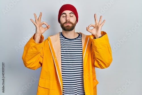 Caucasian man with beard wearing yellow raincoat relaxed and smiling with eyes closed doing meditation gesture with fingers. yoga concept.