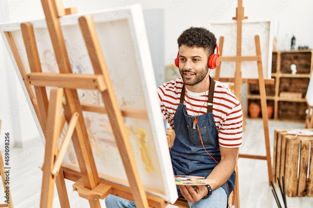 Young arab artist man listening to music drawing at art studio.