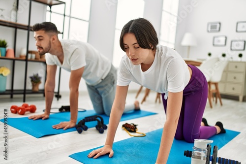 Young hispanic couple doing sport stretching on the mat at home
