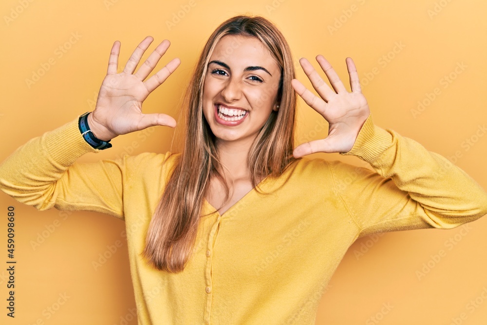 Beautiful hispanic woman wearing casual yellow sweater showing and pointing up with fingers number ten while smiling confident and happy. Beautiful hispanic woman wearing casual yellow sweater showing and pointing up with fingers number ten while smiling confident and happy.