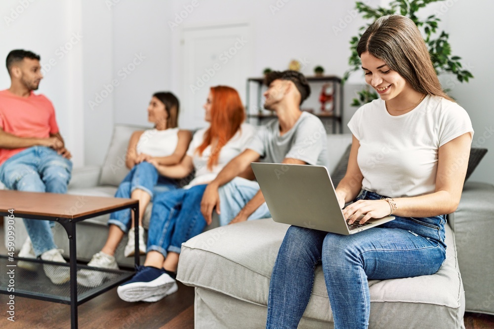 Group of young friends speaking sitting on the sofa. Woman smilimg happy and using laptop at home. Group of young friends speaking sitting on the sofa. Woman smilimg happy and using laptop at home.
