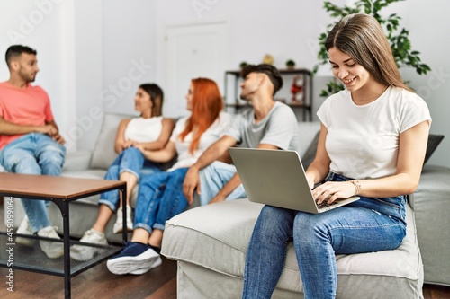 Group of young friends speaking sitting on the sofa. Woman smilimg happy and using laptop at home. © Krakenimages.com