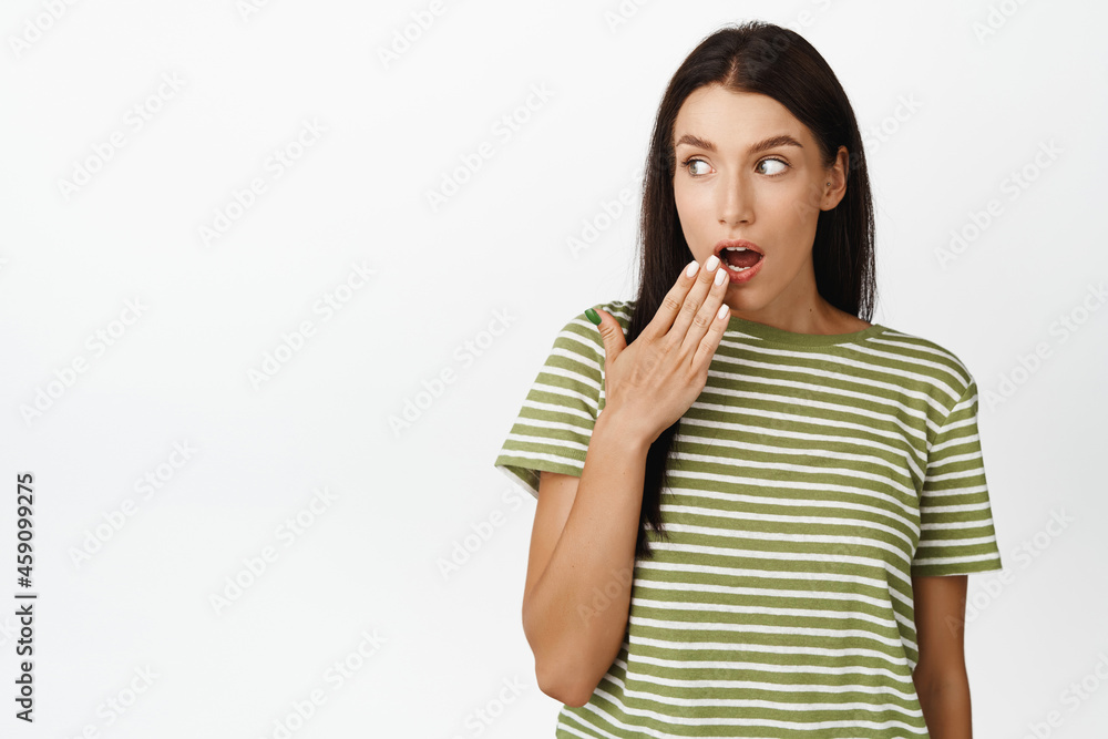 Amazed brunette woman gasping, cover mouth and looking left at promo, hear gossips, standing in t-shirt over white background Amazed brunette woman gasping, cover mouth and looking left at promo, hear gossips, standing in t-shirt over white background