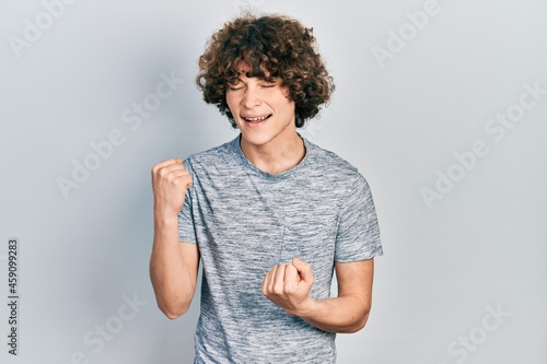 Handsome young man wearing casual grey t shirt celebrating surprised and amazed for success with arms raised and eyes closed