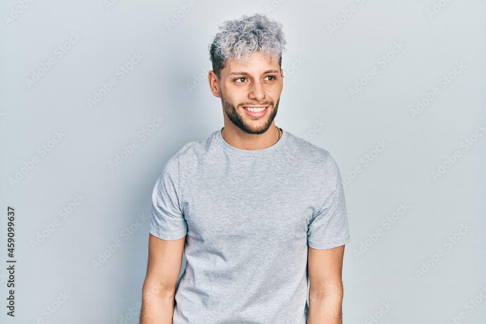 Young hispanic man with modern dyed hair wearing casual grey t shirt looking away to side with smile on face, natural expression. laughing confident. Young hispanic man with modern dyed hair wearing casual grey t shirt looking away to side with smile on face, natural expression. laughing confident.