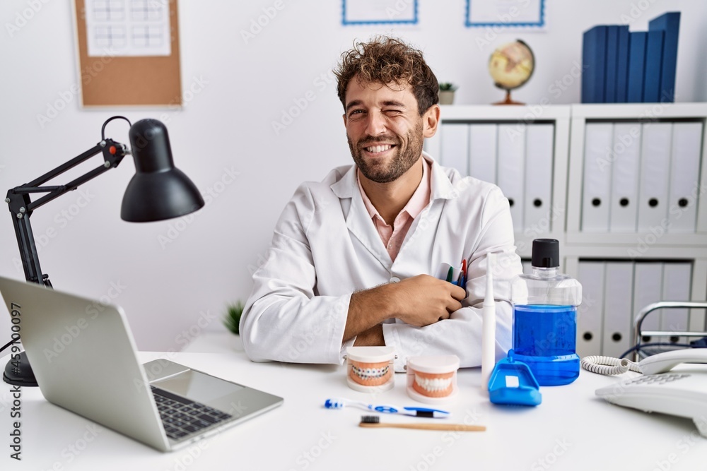 Young hispanic dentist man working at medical clinic winking looking at the camera with sexy expression, cheerful and happy face. Young hispanic dentist man working at medical clinic winking looking at the camera with sexy expression, cheerful and happy face.