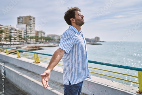 Fototapeta Naklejka Na Ścianę i Meble -  Young hispanic man breathing with arms open standing at the promenade.