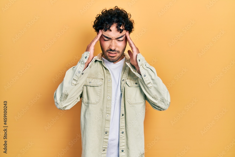 Young hispanic man wearing casual clothes with hand on head for pain in head because stress. suffering migraine. Young hispanic man wearing casual clothes with hand on head for pain in head because stress. suffering migraine.