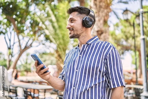 Young handsome man wearing headhphones using smartphone at park photo