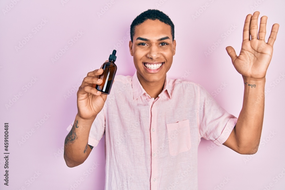 Young african american guy holding serum bottle celebrating achievement with happy smile and winner expression with raised hand Young african american guy holding serum bottle celebrating achievement with happy smile and winner expression with raised hand