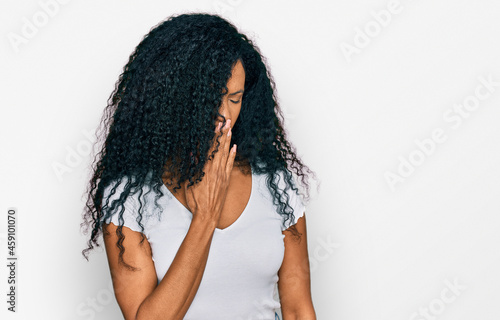 Middle age african american woman wearing casual white t shirt bored yawning tired covering mouth with hand. restless and sleepiness.