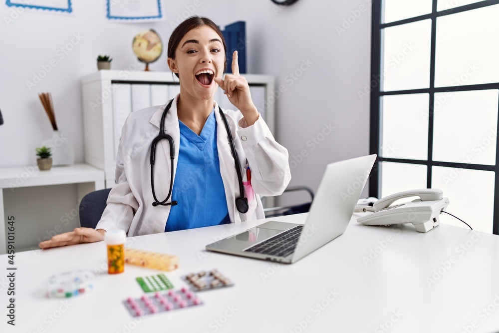 Obraz premium Young hispanic doctor woman wearing doctor uniform working at the clinic pointing finger up with successful idea. exited and happy. number one.