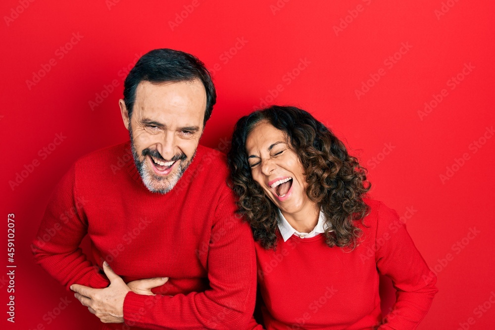 Middle age couple of hispanic woman and man hugging and standing together smiling and laughing hard out loud because funny crazy joke with hands on body. Middle age couple of hispanic woman and man hugging and standing together smiling and laughing hard out loud because funny crazy joke with hands on body.