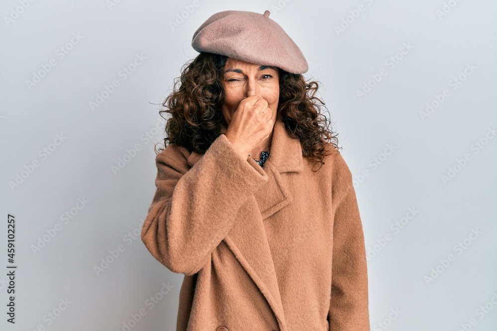 Middle age hispanic woman wearing french look with beret smelling something stinky and disgusting, intolerable smell, holding breath with fingers on nose. bad smell Middle age hispanic woman wearing french look with beret smelling something stinky and disgusting, intolerable smell, holding breath with fingers on nose. bad smell