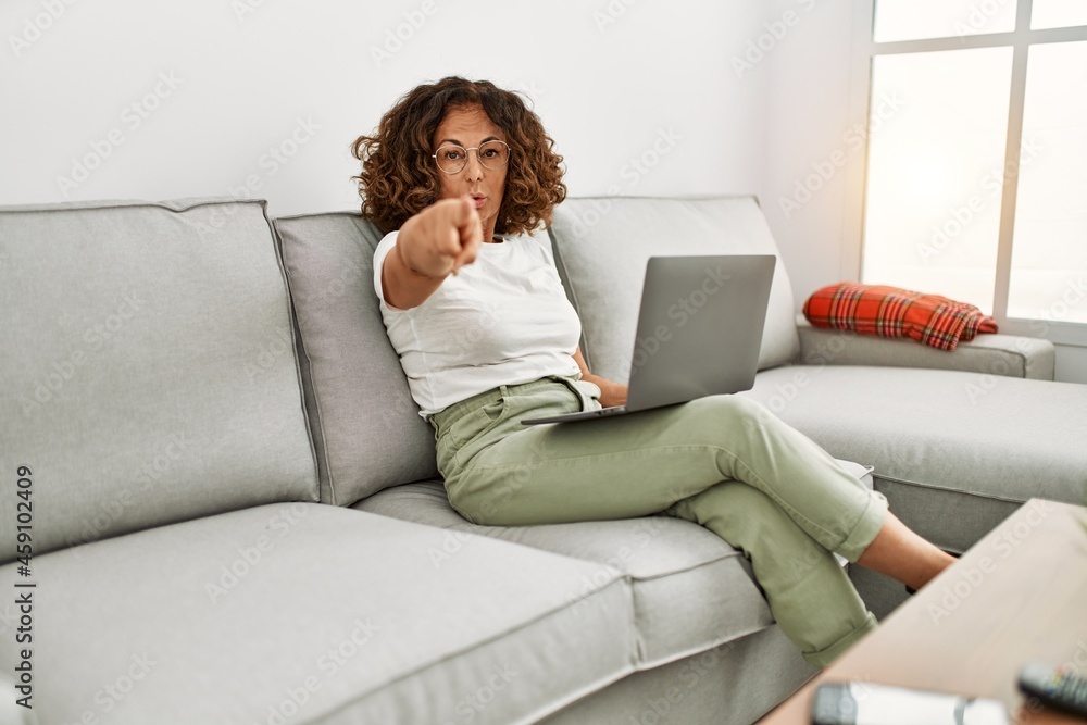 Middle age hispanic woman working using computer laptop at home pointing with finger to the camera and to you, confident gesture looking serious Middle age hispanic woman working using computer laptop at home pointing with finger to the camera and to you, confident gesture looking serious