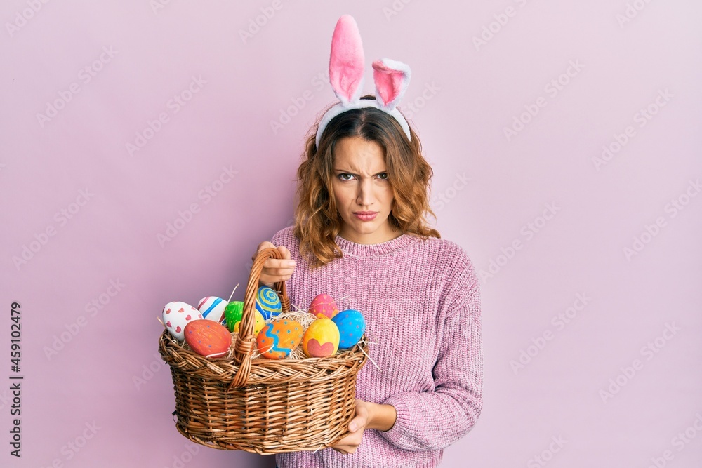 Young caucasian woman wearing cute easter bunny ears holding colored egg skeptic and nervous, frowning upset because of problem. negative person.