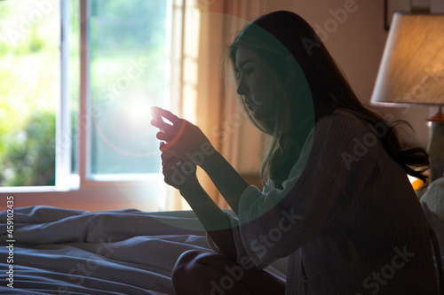 Dark and blurry images of a lonely sexy Asian woman with long hair texting in the dark on her cell phone or checking her social media in a cozy room until morning. Social media and internet concept