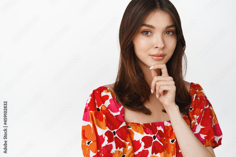 Portrait of beautiful brunette woman gazing at camera thoughtful, wearing stylish floral dress, standing over white background Portrait of beautiful brunette woman gazing at camera thoughtful, wearing stylish floral dress, standing over white background