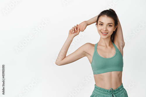 Smiling female athlete stretching arms, warm-up in gym before workout, showing fitness exercises, white background