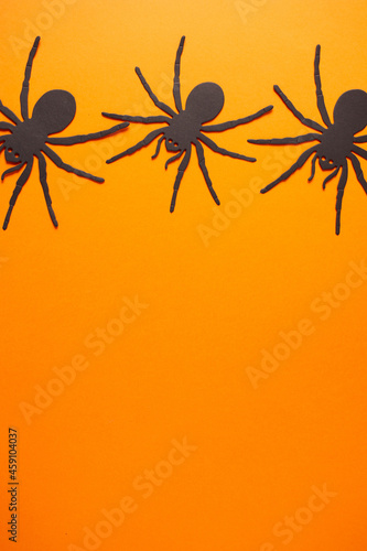 Vibrant orange background with metallic black widow spiders on top with copy space