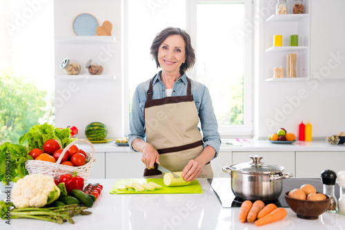 Photo of cheerful positive old woman smile good mood cut vegetables smile indoors inside house home kitchen