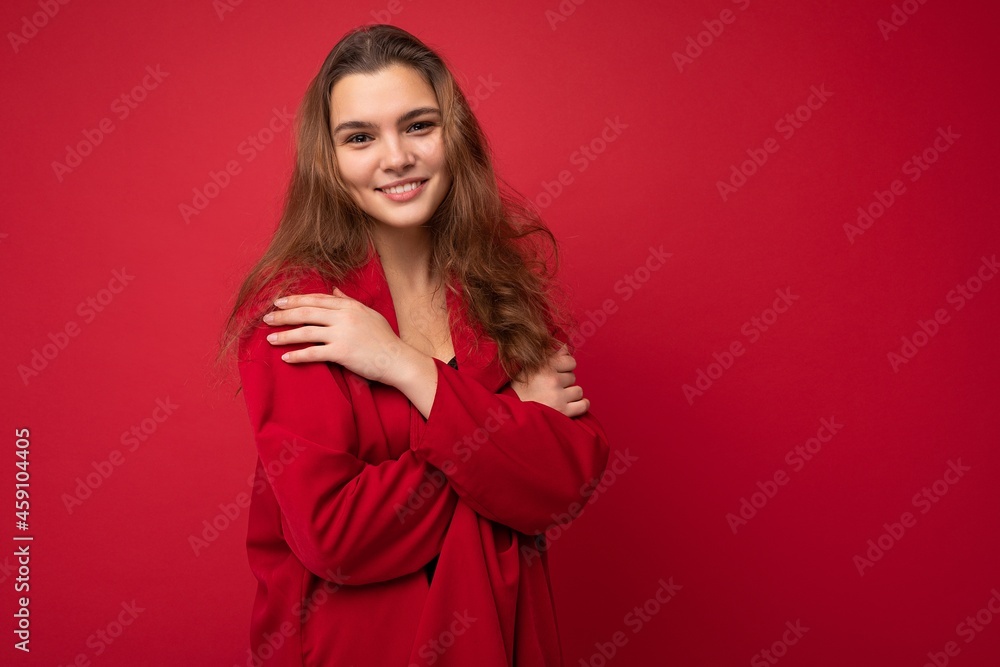 Fototapeta premium Portrait of young attractive caucasian hipster woman in trendy casual clothes. Sexy carefree female person posing isolated near red wall in studio. Positive model with natural makeup. Empty space