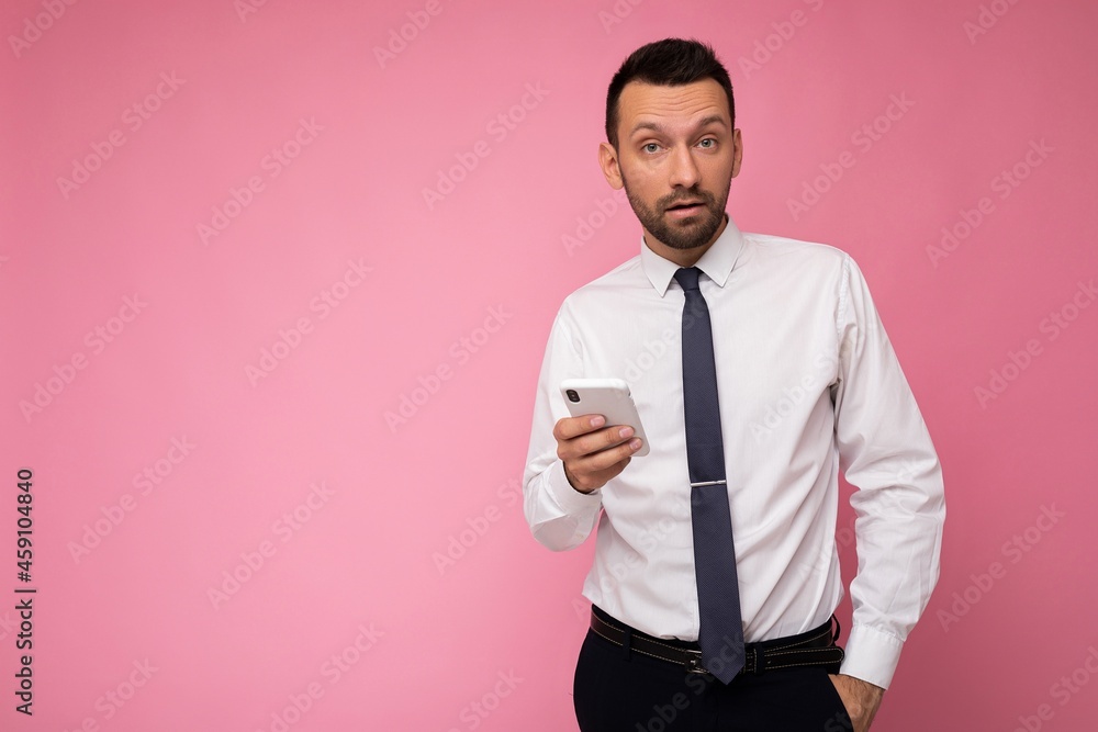 Photo of handsome good looking man wearing casual white shirt and tie isolated on pink background with empty space holding in hand and using mobile phone messaging sms looking at camera Photo of handsome good looking man wearing casual white shirt and tie isolated on pink background with empty space holding in hand and using mobile phone messaging sms looking at camera