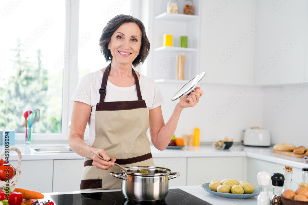 Photo of optimistic agee brunette lady cook potatoes wear apron white t-shirt at kitchen alone Photo of optimistic agee brunette lady cook potatoes wear apron white t-shirt at kitchen alone