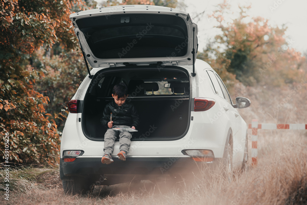 A child is sitting in the trunk of a car SUV or crossover with gouache paints, a car in the autumn forest