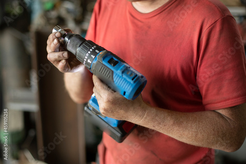 The man shows a screwdriver. A guy in a workshop with a power tool in his hand.