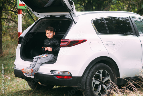 A child is sitting in the trunk of a car SUV or crossover with gouache paints, a car in the autumn forest