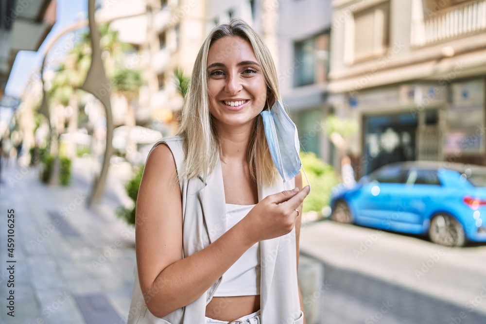 Young blonde girl wearing medical mask holding covid-19 vaccination record card at the city. Young blonde girl wearing medical mask holding covid-19 vaccination record card at the city.