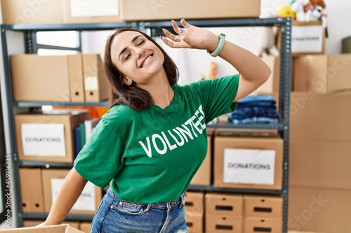 Young brunette woman wearing volunteer t shirt at donations stand dancing happy and cheerful, smiling moving casual and confident listening to music