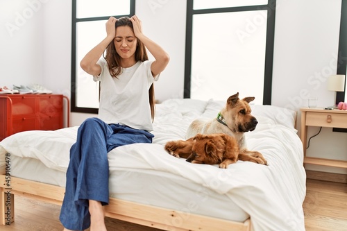 Canvas Print Young brunette woman sitting on the bed with two dogs suffering from headache desperate and stressed because pain and migraine