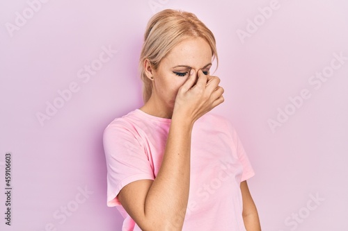 Young blonde woman wearing casual pink t shirt tired rubbing nose and eyes feeling fatigue and headache. stress and frustration concept.