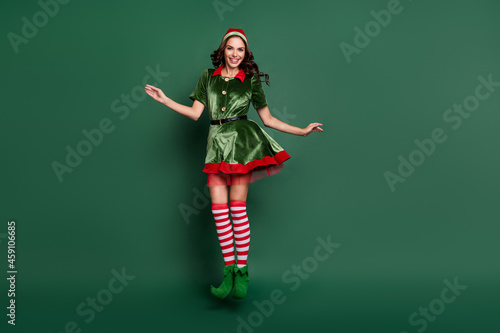 Full length photo of young girl elf happy positive smile jump up christmas time holiday isolated over green color background