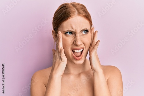 Young irish woman standing topless stretching skin face with hands angry and mad screaming frustrated and furious, shouting with anger. rage and aggressive concept.